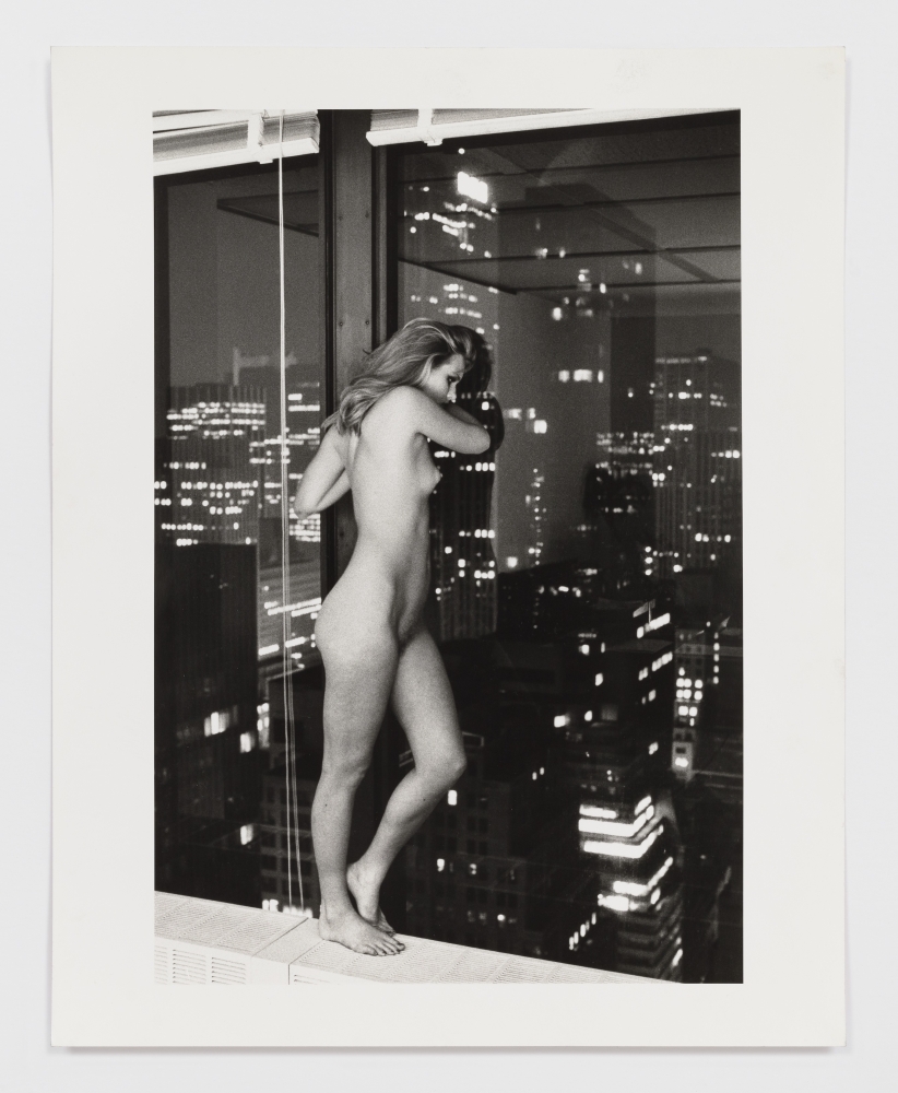 Black and white photographic print of Patti Hansen standing nude and overlooking Manhattan from a window