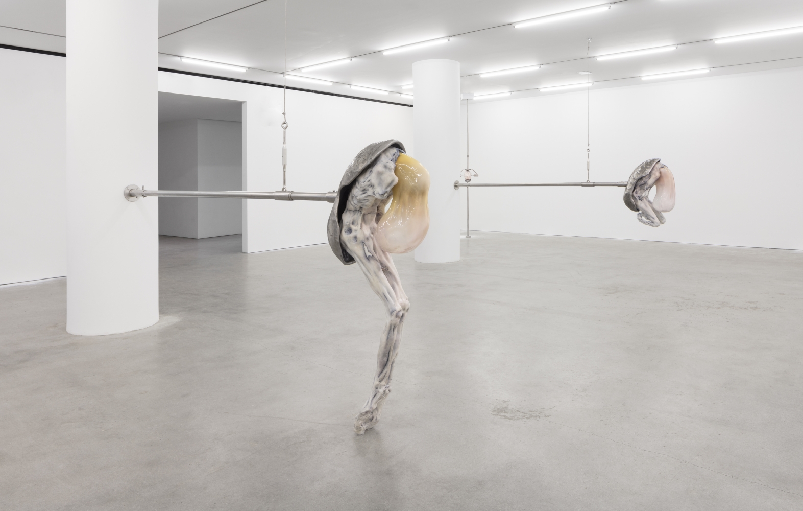 Installation shot of two humanoid figures emerging from oval shell attached by stainless steel rod in an Ivana Bašić exhibition.