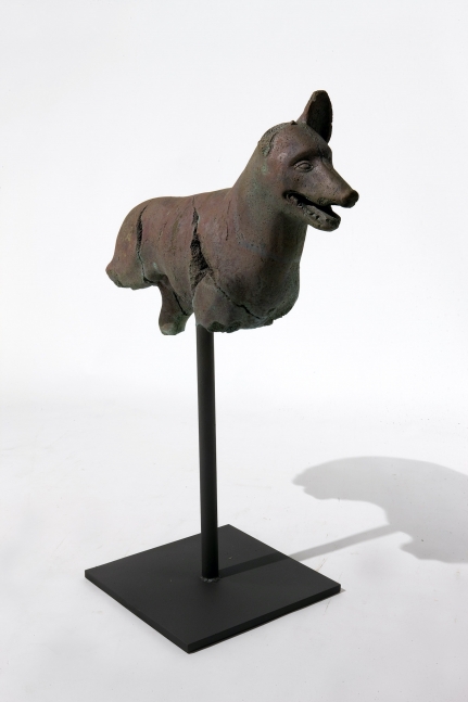 Rusted and fragmented bronze dog statue atop a steel rod.