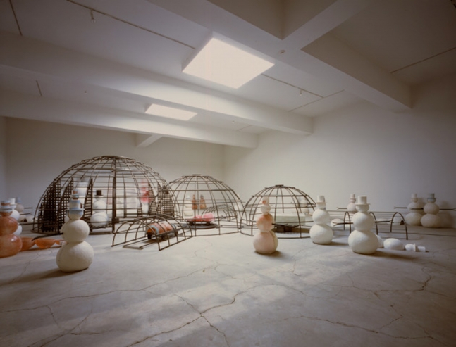 Installation shot of Dennis Oppenheim's cluster of white and pink snowmen alongside caged steel igloos.