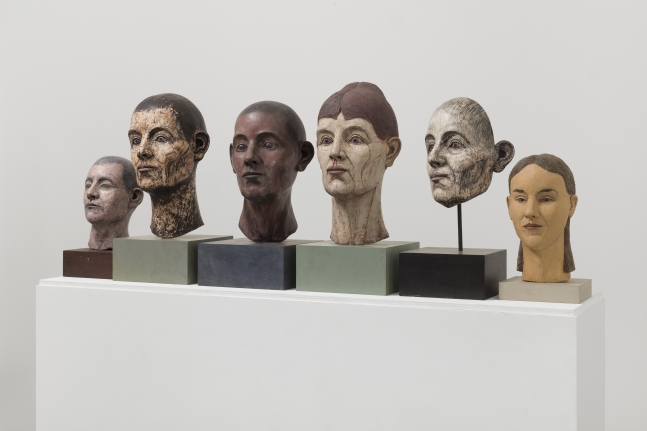 Side-view photograph featuring group of six different sculptural heads ranging in size, gender and color