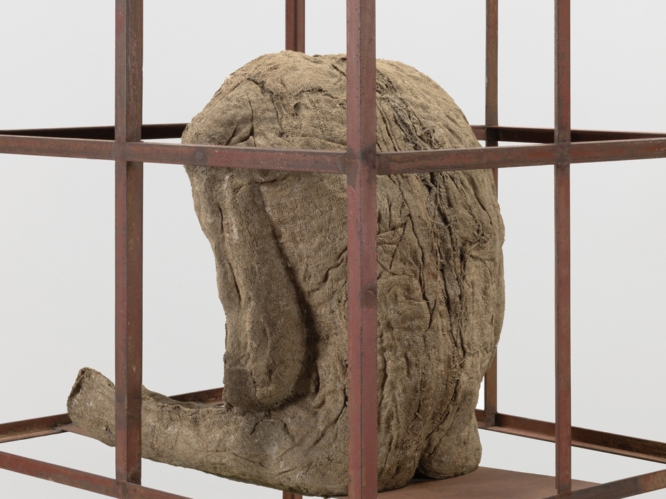 Sculpture of a life-size seated burlap and resin figure in an iron cage by Magdalena Abakanowicz