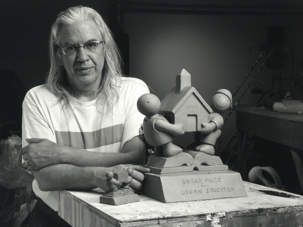 Black and white photographic portrait of Tom Otterness in his studio with model for Broad Prize for Urban Education